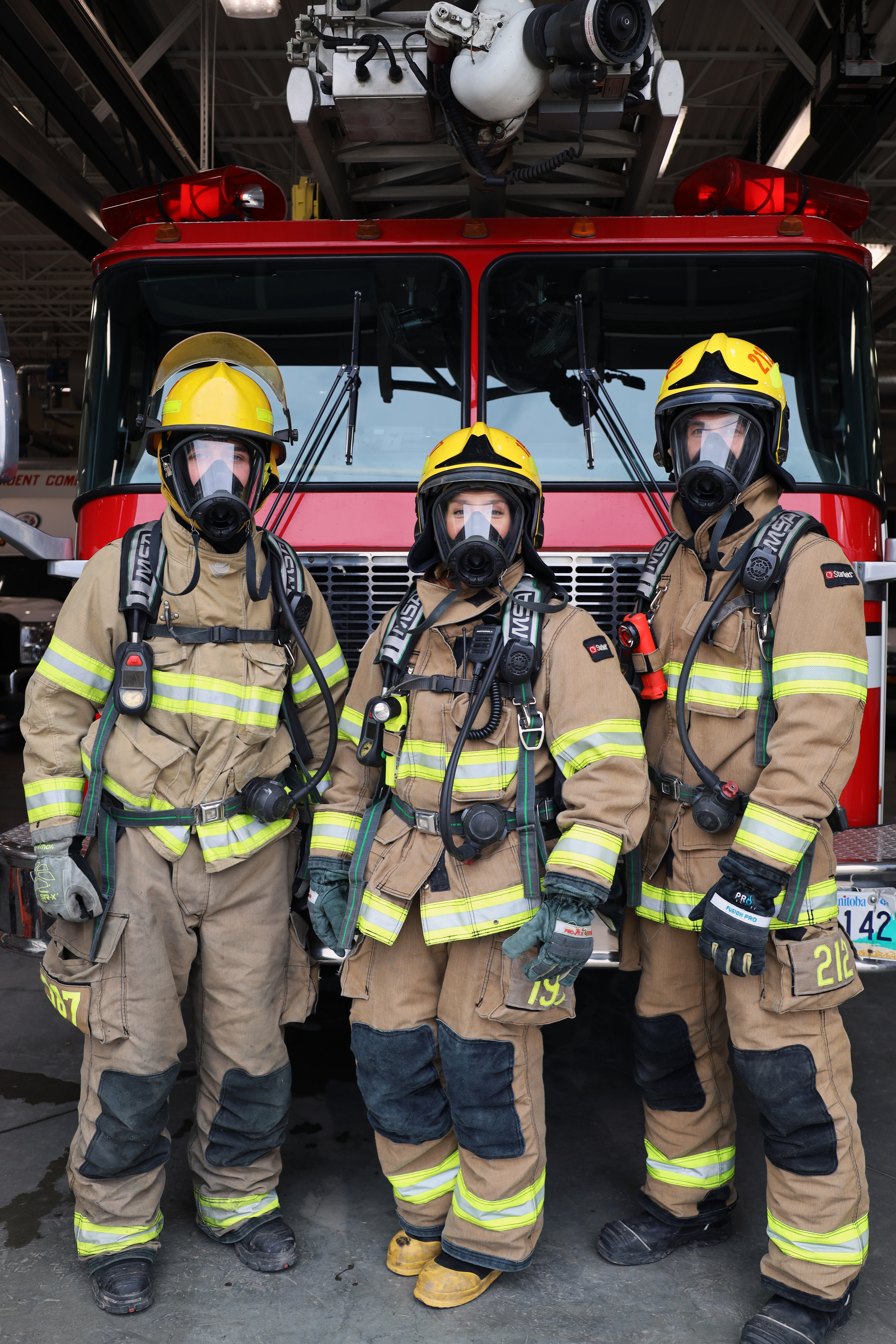 Three firefighters in front of the engine wearing gear.
