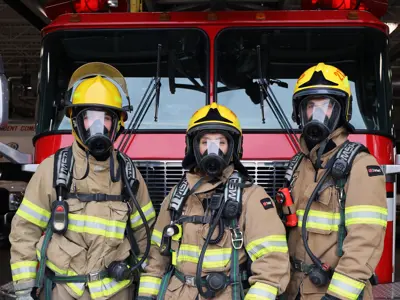 Three firefighters in front of the engine wearing gear.